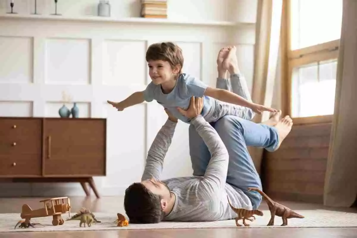 Un père soulève les bras et les pieds de son fils comme un avion